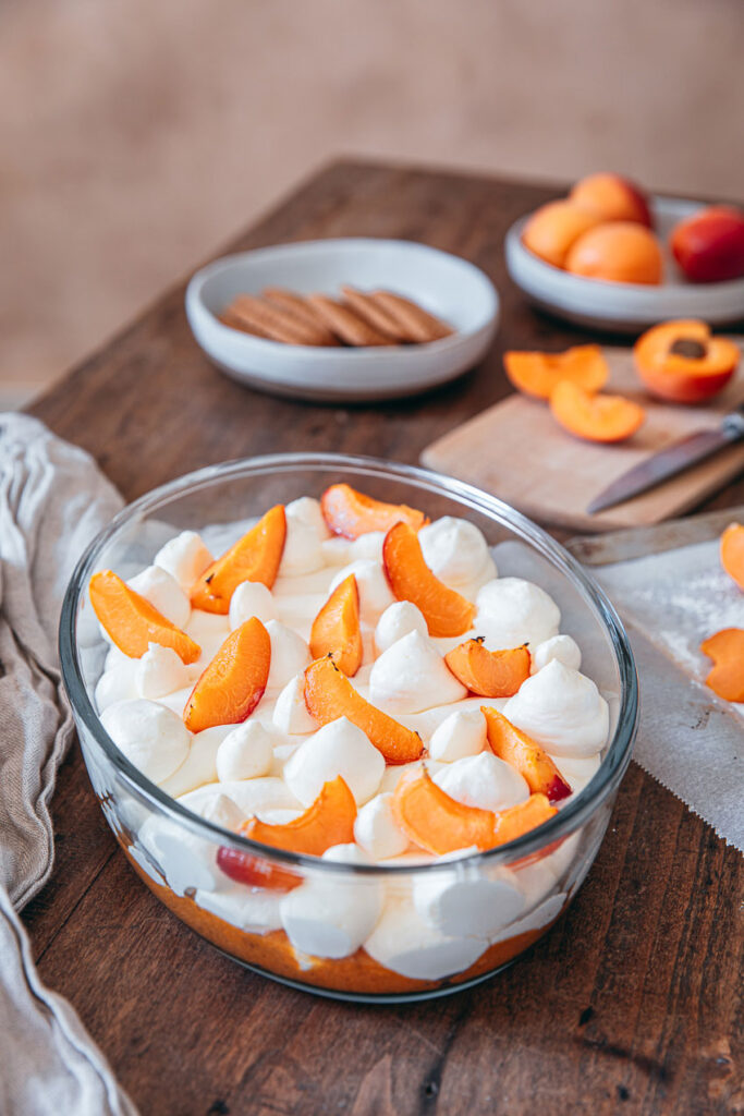 Tiramisu spéculoos abricots frais servi dans un plat en verre, garni de crème mascarpone, morceaux de spéculoos et quartiers d’abricots sur une table en bois.