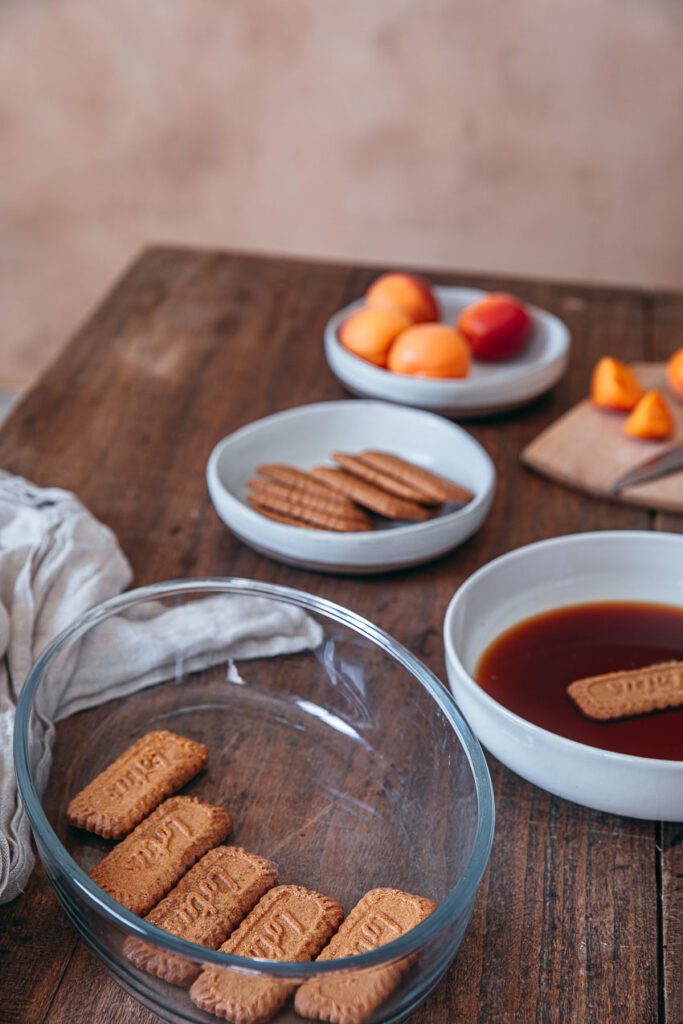 Tiramisu spéculoos abricots frais servi dans un plat en verre, garni de crème mascarpone, morceaux de spéculoos et quartiers d’abricots sur une table en bois.